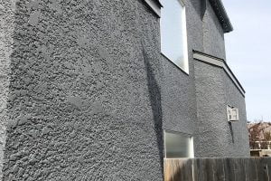 Close-up of a modern house with a rough gray stucco facade and rectangular windows.